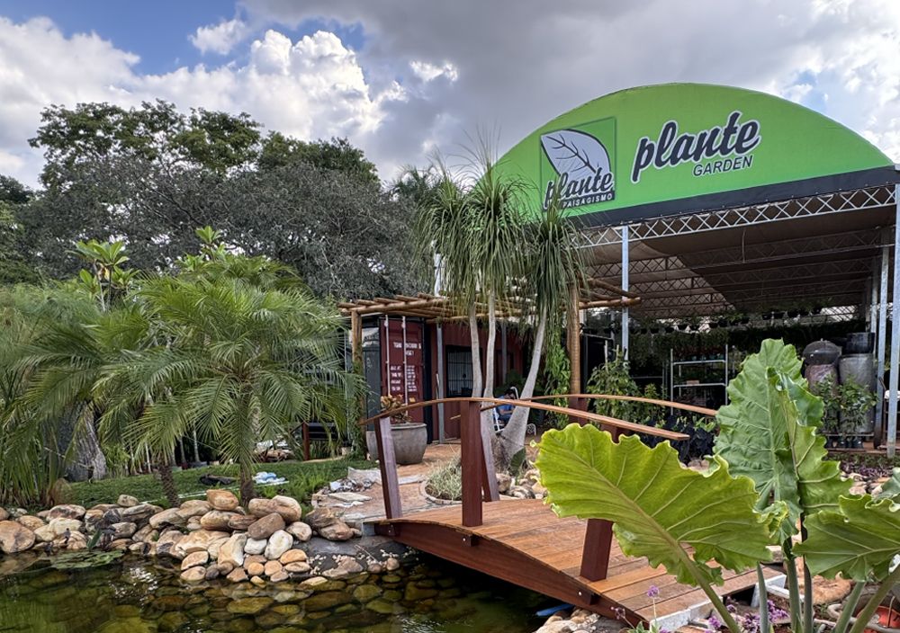 Fachada da Plante Garden: tenda verde, lago com ponte de madeira e jardim paisagístico